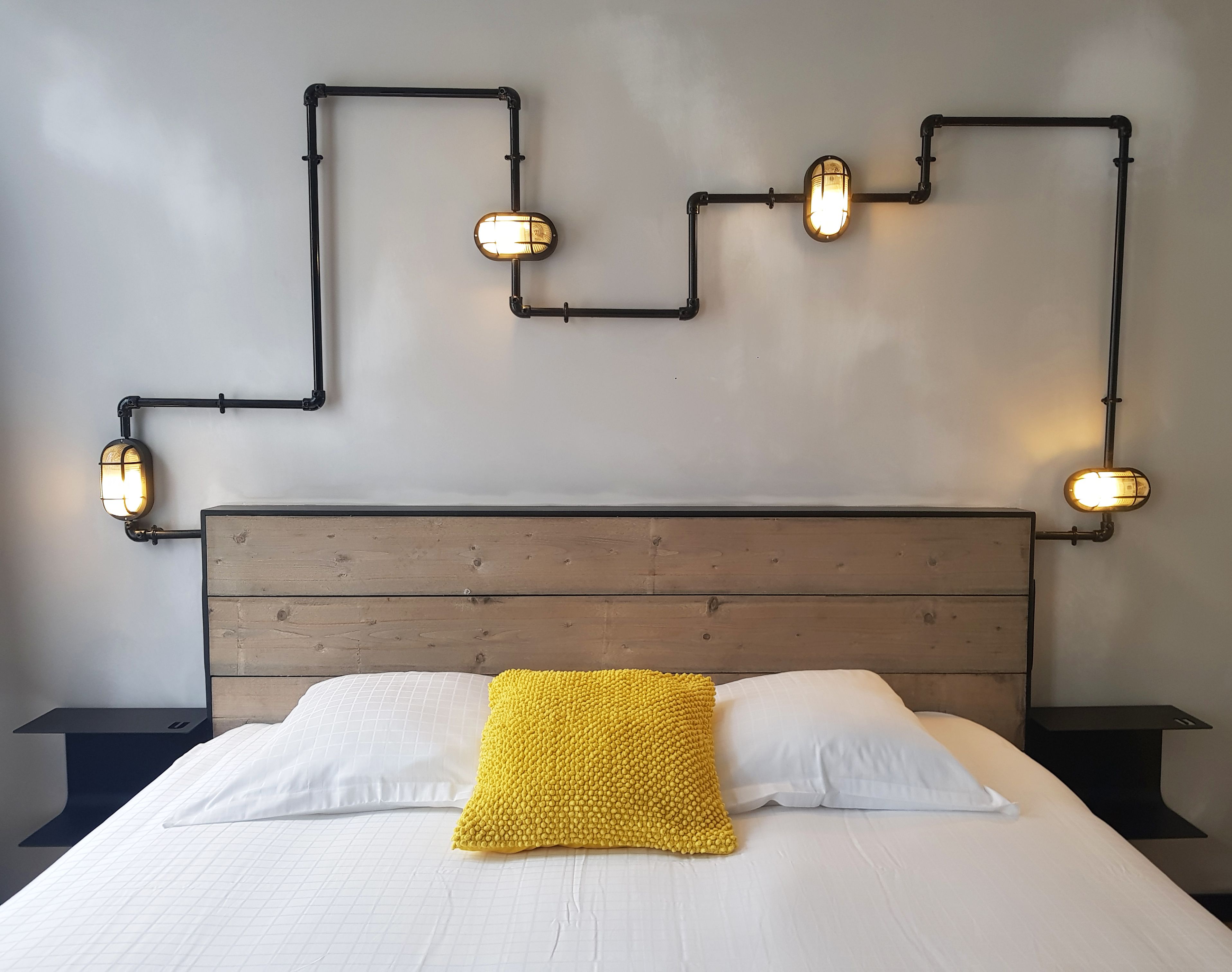 Una cama con cabecera de madera, ropa de cama blanca y una manta amarilla.