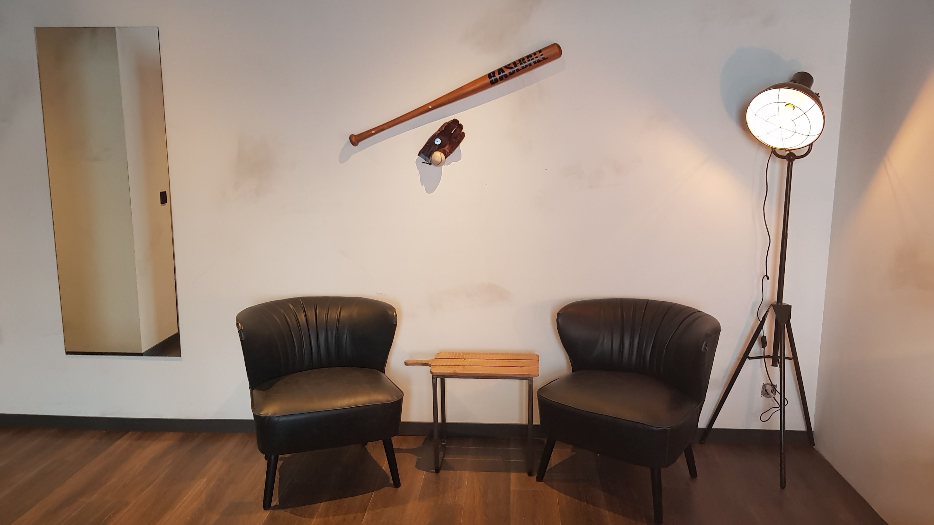 Una stanza con due poltrone in pelle, un tavolino, una mazza da baseball, un guanto e una lampada da terra.