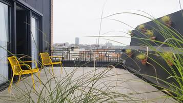 A balcony with yellow chairs, potted plants, and a city view.