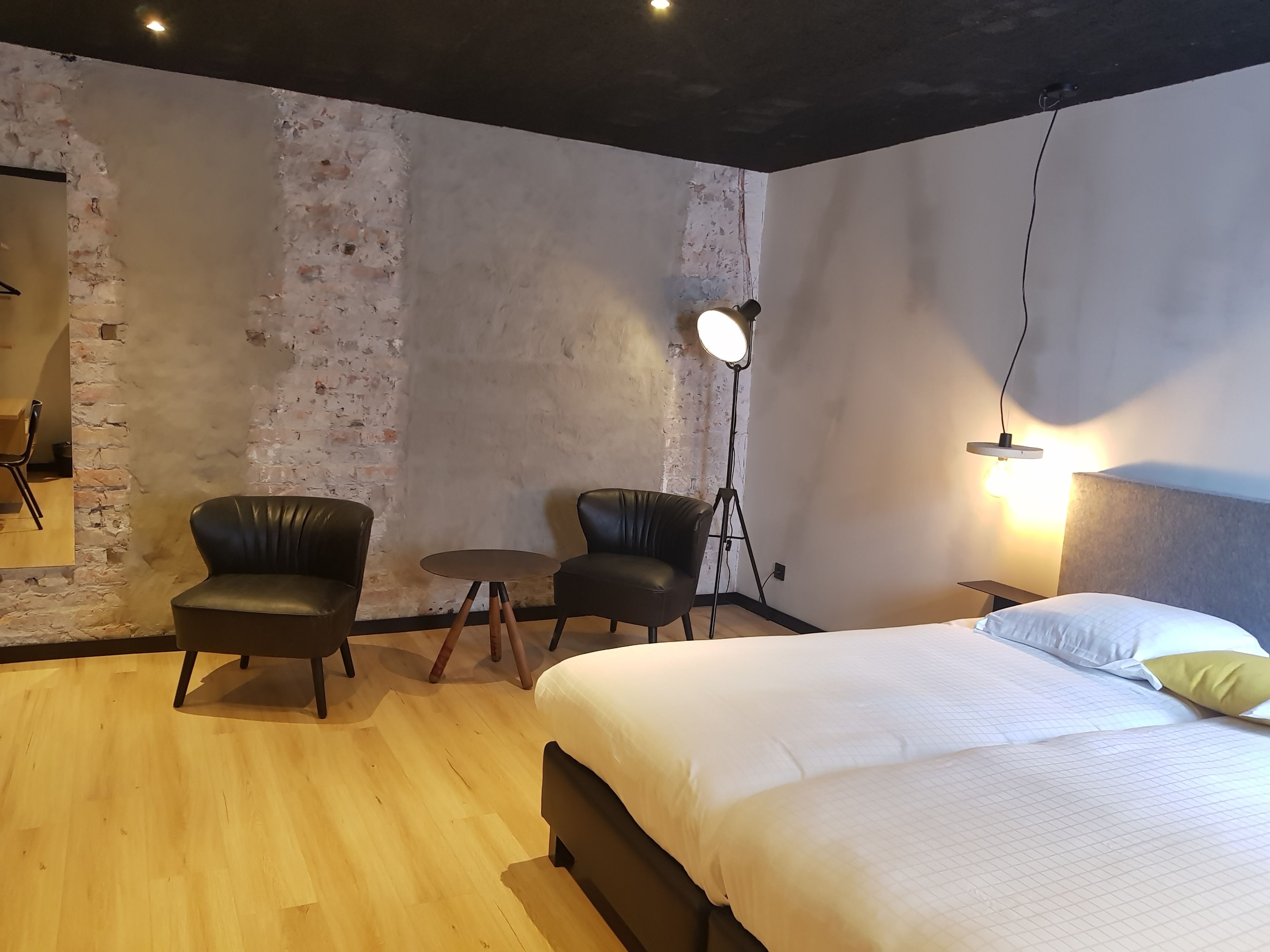 Una habitación de hotel con una cama, dos sillones de cuero, una mesita y una lámpara de pie.