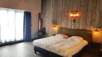 Une chambre à coucher avec une tête de lit en bois, un lit avec une literie blanche, deux lampes de chevet, une table de chevet et une grande fenêtre avec des rideaux.