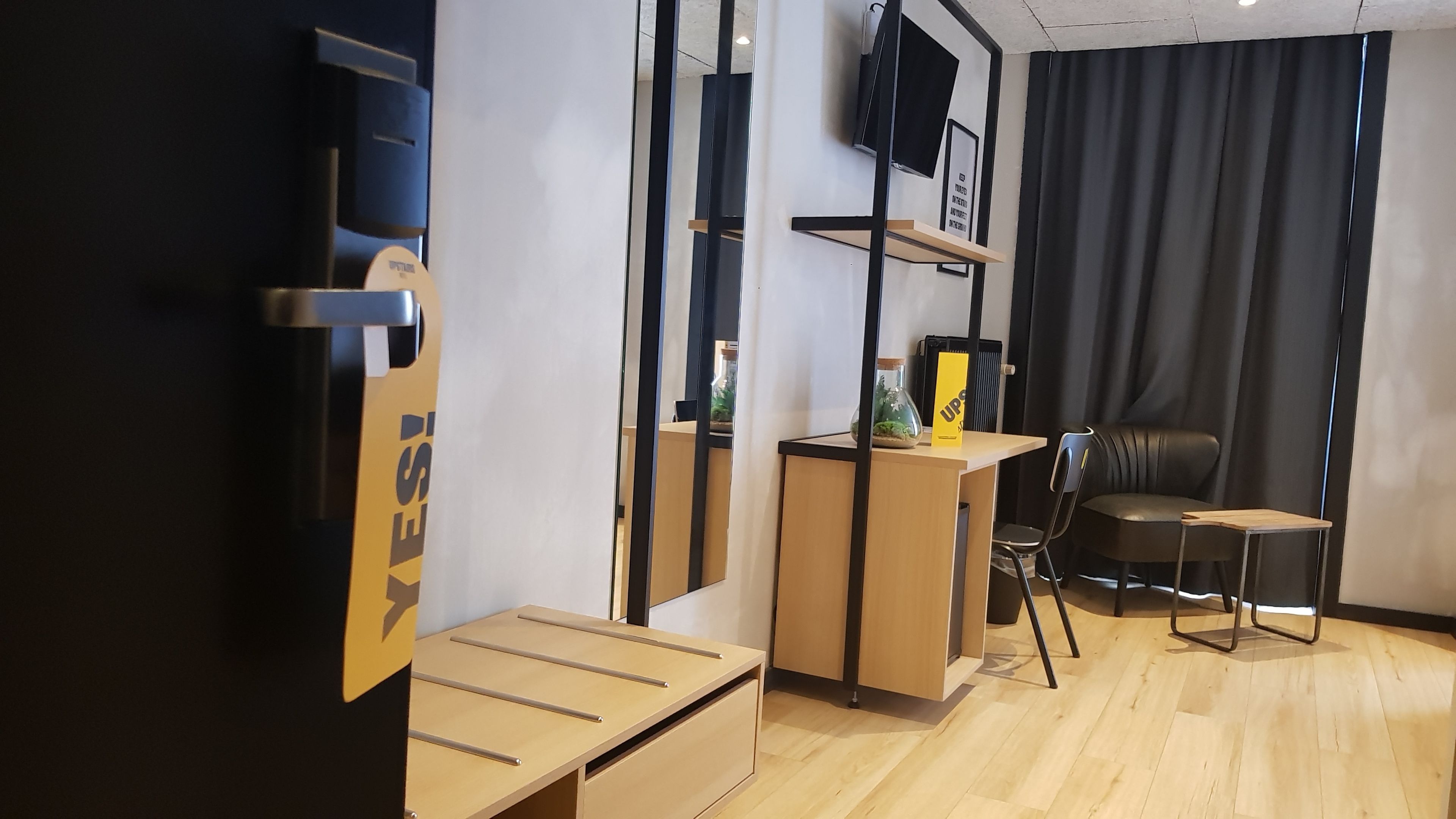 Una habitación de hotel moderna con un escritorio de madera, una silla, una mesita, un espejo y un televisor montado en la pared.