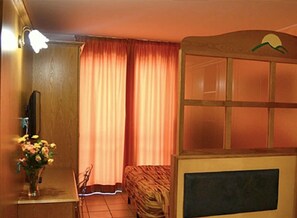 A room with a bed, a small desk with a television, a vase of flowers, and a window with curtains. - Alba Sporting Hotel (Rocca di Mezzo)