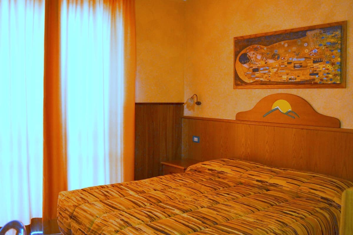 A hotel room with a bed, a wooden headboard, a painting on the wall, and a window with curtains.