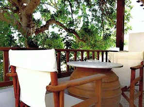 An outdoor seating area with a round table and wooden chairs, surrounded by a wooden railing and a large tree.