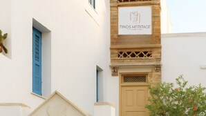 A building with a staircase, a wooden door, and a sign reading "Tinos Heritage." - Tinos Heritage Plateia (Tinos)