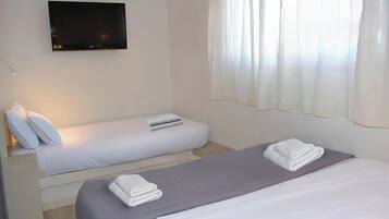 Habitación de hotel con dos camas, un televisor de pantalla plana montado en la pared y cortinas translúcidas en la ventana.