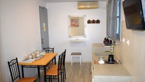 A compact kitchen with a dining area, a small window, and a mounted TV. - Tinos Heritage Plateia (Tinos)
