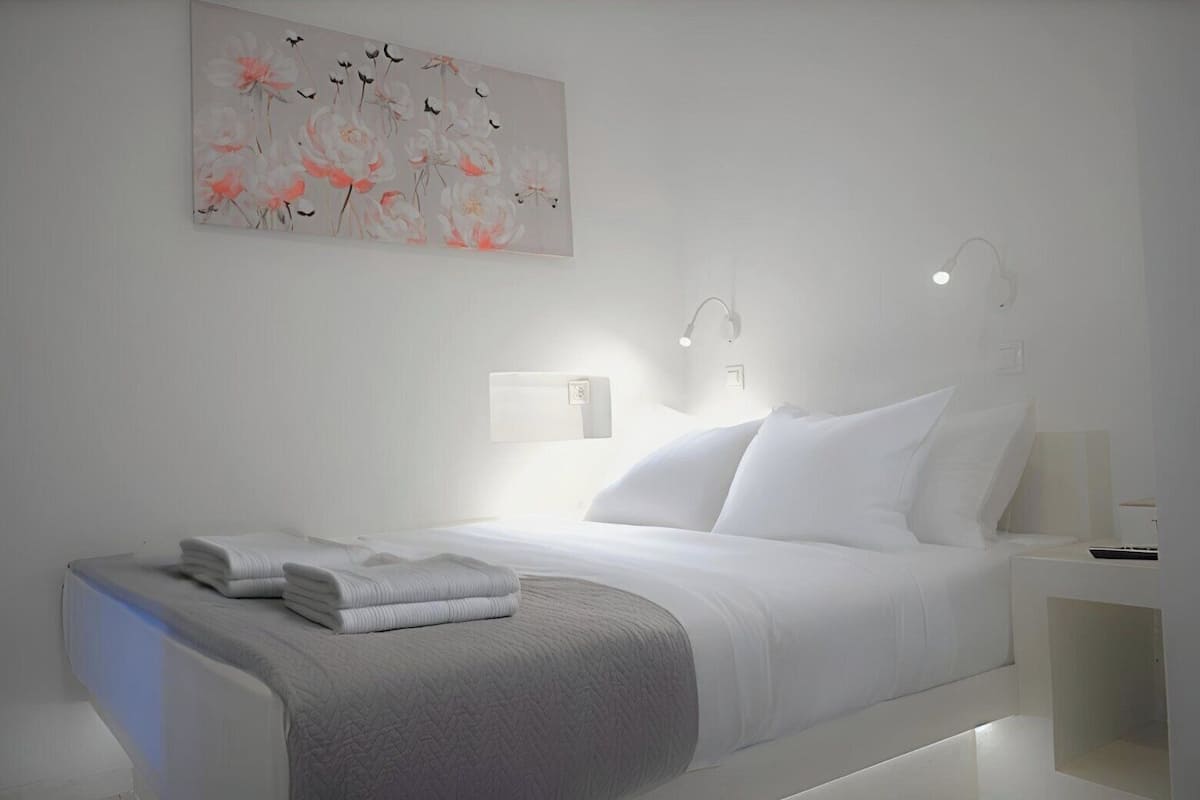 Una habitación de hotel moderna con una cama bien hecha, una mesita de noche con lámpara y una obra de arte colgada en la pared.