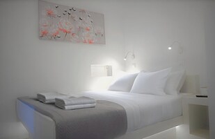 Quarto de hotel moderno com cama bem arrumada, mesa de cabeceira com abajur e uma obra de arte na parede.