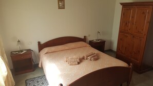 Un dormitorio con cama de madera, una mesita de noche con lámpara, un armario y un tapete estampado en el suelo.