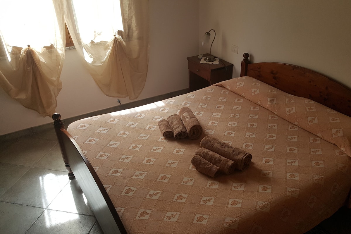 A bedroom with a bed, a nightstand, a lamp, and a window with curtains.