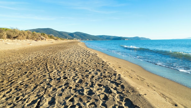 A sandy beach with footprints leading to the water, a clear sky, and distant mountains. - Agriturismo Al Vermigliano (Grosseto)