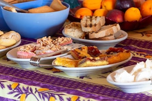 Een tafel met diverse etenswaren, zoals brood, gebak en fruit.