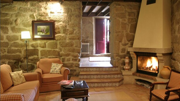A cozy stone-floored living room with a fireplace, checkered sofas, and a lamp. - Hotel O Portelo Rural (Allariz)