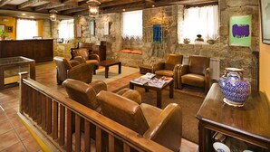 A cozy lounge area with leather sofas, a wooden coffee table, and stone walls. - Hotel O Portelo Rural (Allariz)
