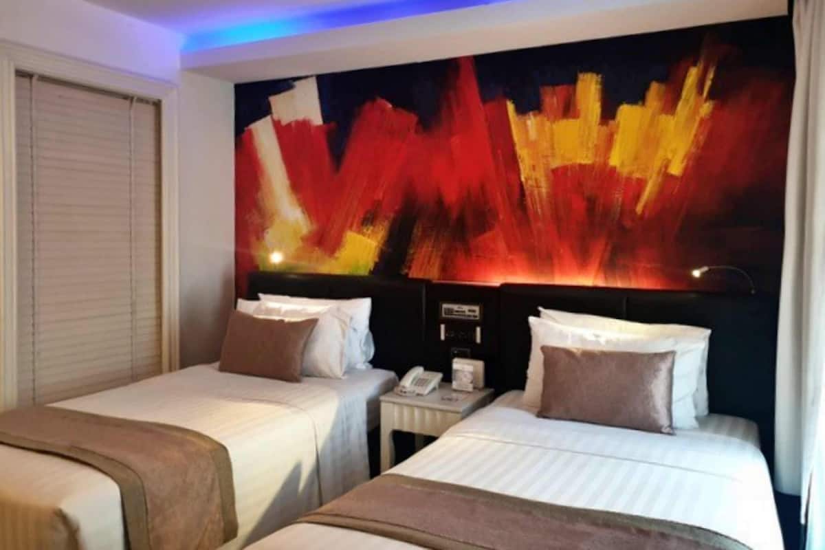 Ein Hotelzimmer mit zwei Betten, einem Nachttisch mit Telefon und einem großen, abstrakten Gemälde an der Wand.