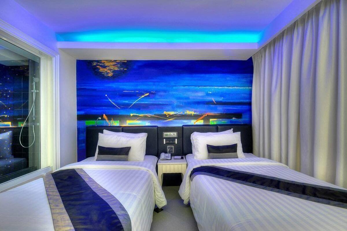 Ein Hotelzimmer mit zwei Betten, Wandmalerei mit Nachthimmel und Blick auf die nächtliche Stadt.