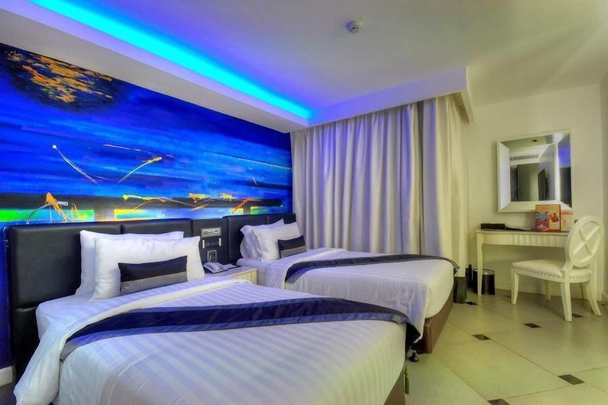 Ein Hotelzimmer mit zwei Betten, einem Schreibtisch, einem Stuhl und einem großen Stadtbild.