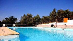 Ein Schwimmbecken mit klarem, blauem Wasser, umgeben von weißen Liegestühlen und einer Holzterrasse.