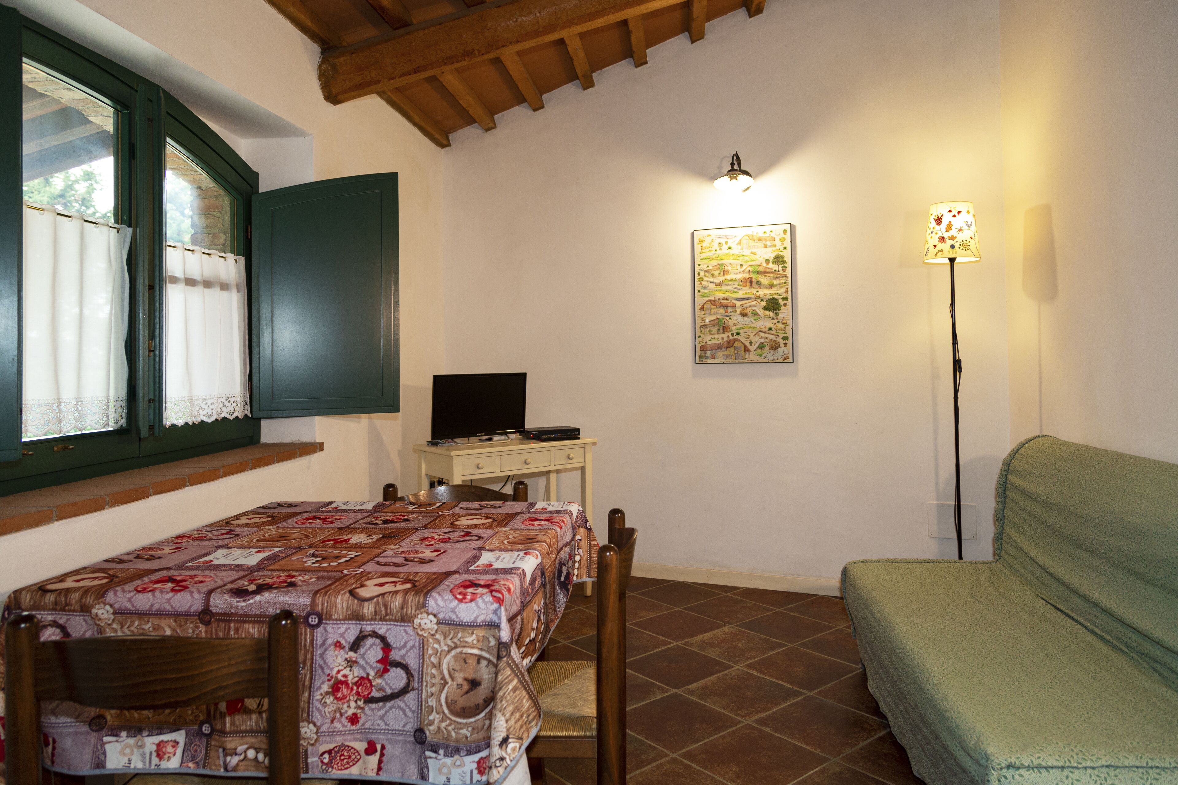 Um quarto com uma cama, uma escrivaninha com computador, uma luminária e um quadro na parede.