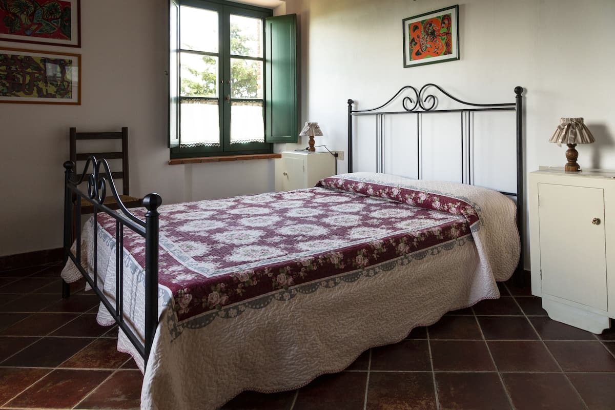 Une chambre à coucher avec un lit, une fenêtre, une chaise, une armoire et des œuvres d’art accrochées aux murs.