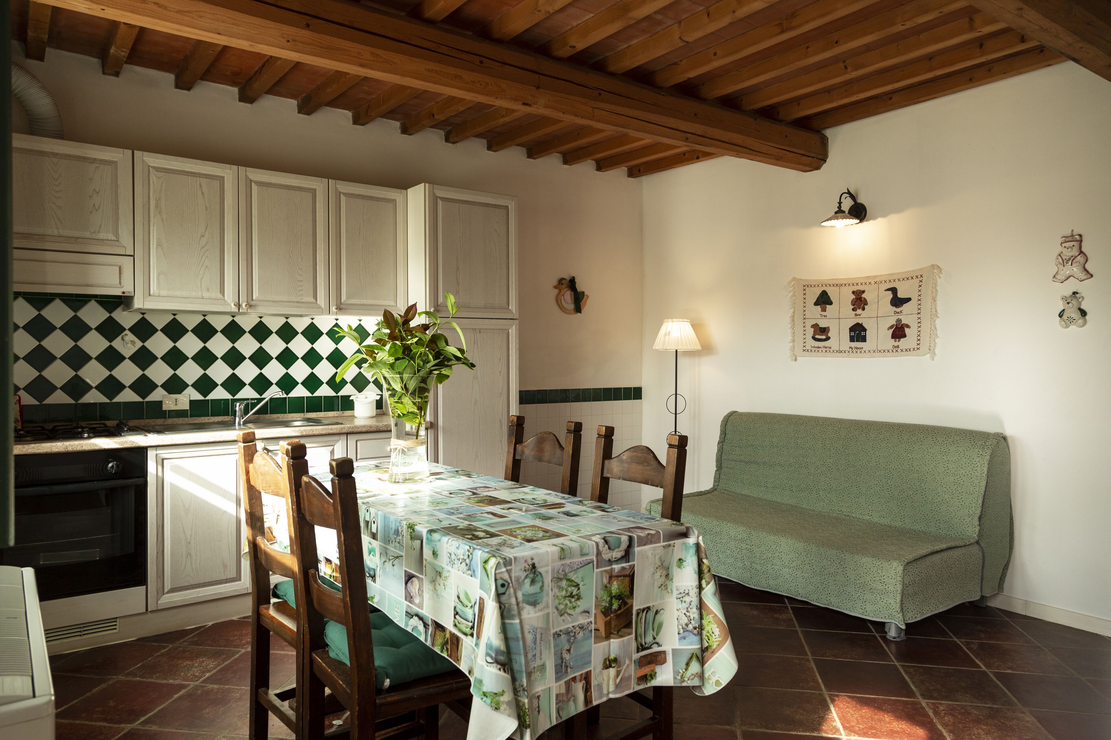 A kitchen with white cabinets, a green and white checkered backsplash, a dining table with a quilted tablecloth, and a green sofa.