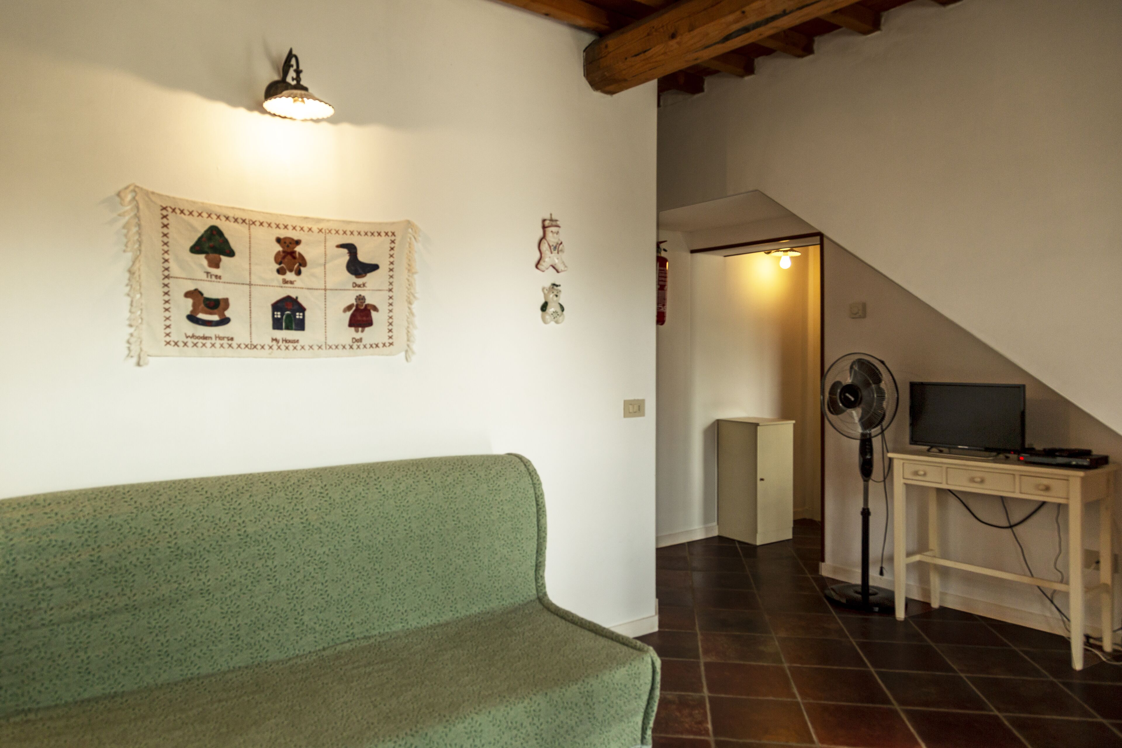 Ein Zimmer mit einem grünen Sofa, einer Wandleuchte, einem Ventilator und einem Fernseher auf einem Holztisch.