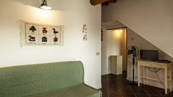 Ein Zimmer mit einem grünen Sofa, einer Wandleuchte, einem Ventilator und einem Fernseher auf einem Holztisch.