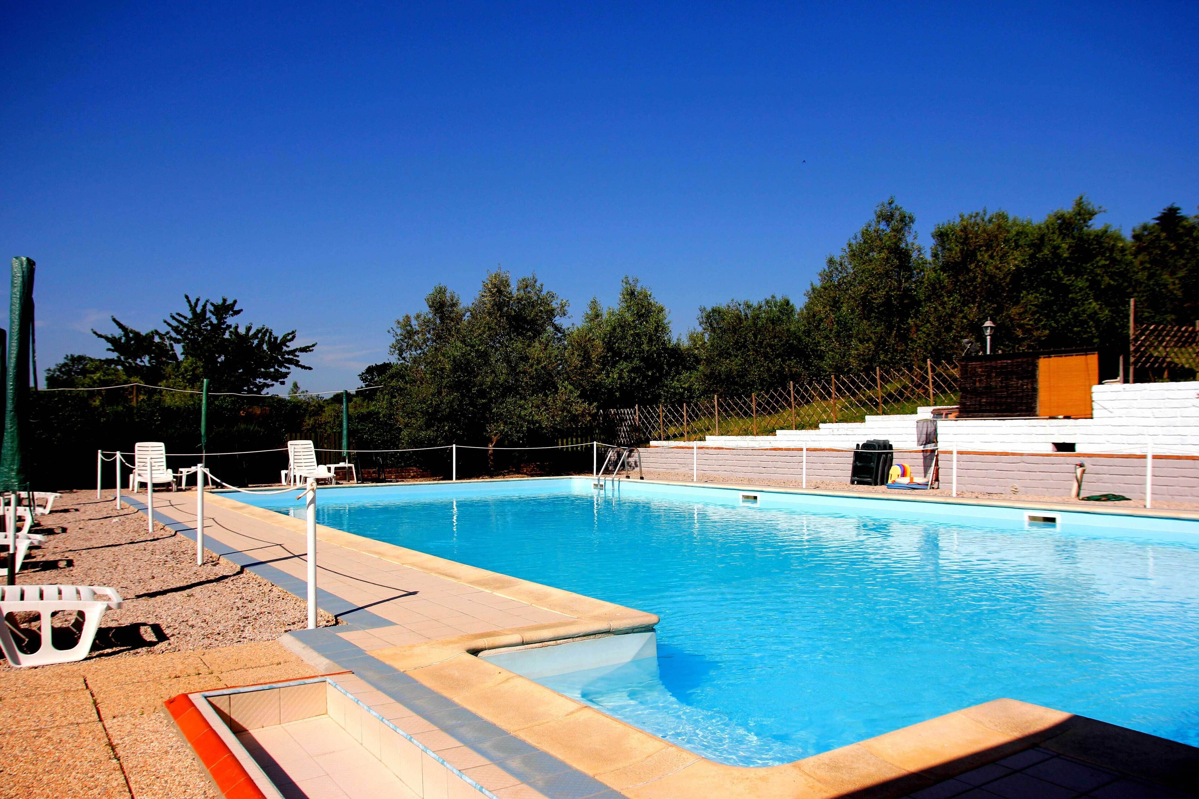 A swimming pool with a tiled deck, lounge chairs, and a fenced area.