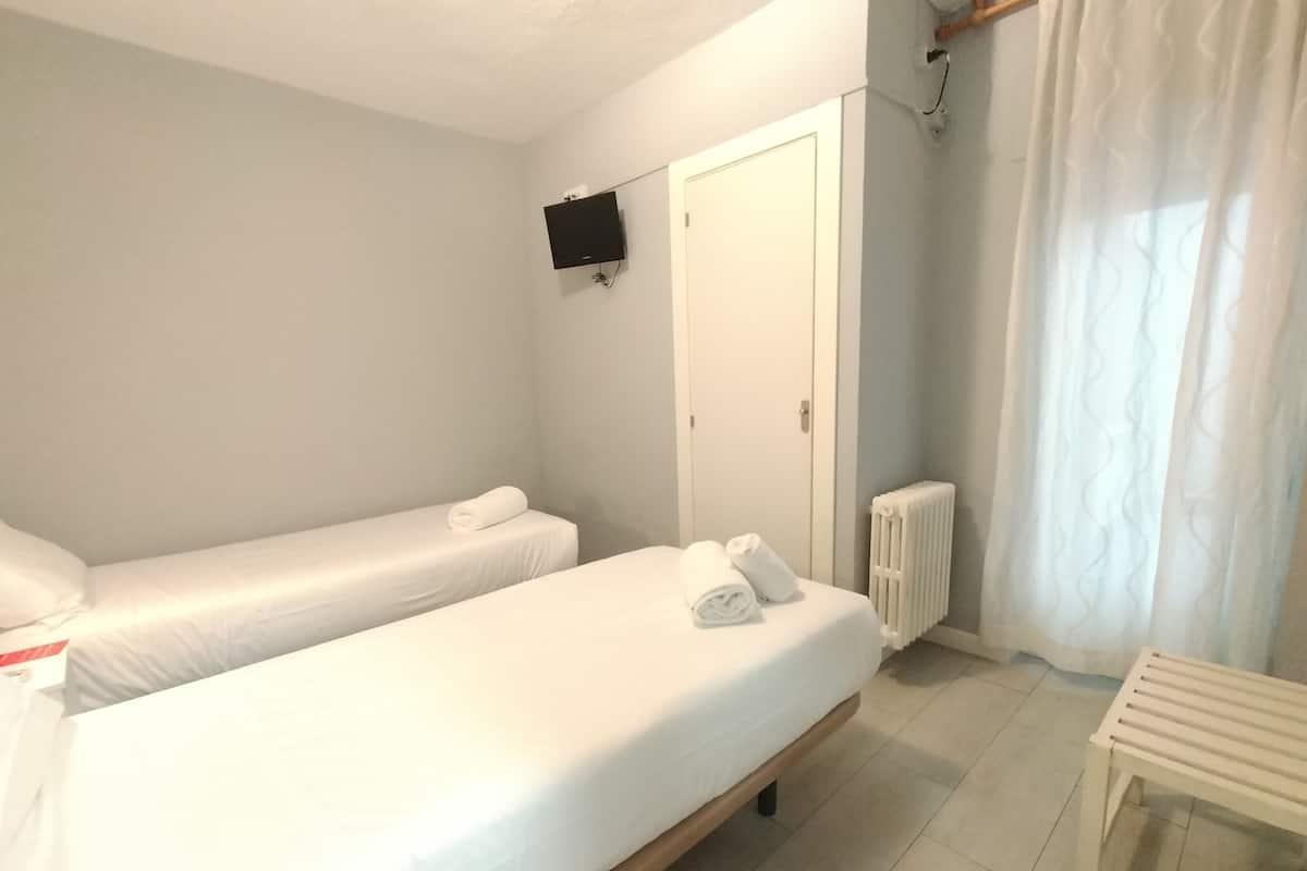 A bedroom with two single beds, a white radiator, a small table, and a TV mounted on the wall.