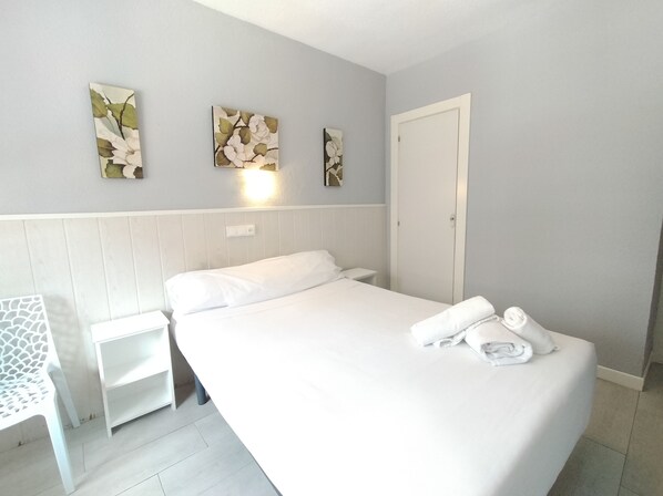 Una habitación de hotel con una cama grande, una mesita de noche pequeña y una obra de arte colgada en la pared.