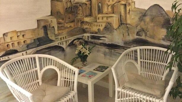 A mural of a historic building, two white wicker chairs, and a small table with a vase of flowers. - Hostal Albero by gaiarooms (Salamanca)