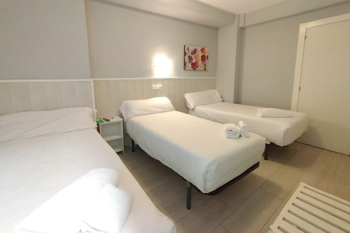 A hotel room with two single beds, a nightstand, a wall-mounted light, and a door.