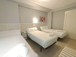 Una habitación de hotel con dos camas individuales, una mesita de noche, una lámpara de pared y una puerta.