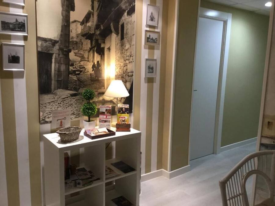 Un pasillo con un mural de piedra, una pequeña mesa con lámpara, cuadros enmarcados y una puerta.