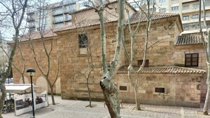 A courtyard with a stone building, a café, and trees. - Hostal Albero by gaiarooms (Salamanca)