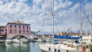 A marina with several boats docked, a pink building with a bridge, and a crane in the background. - Stunning apartment in Genova (GE) (Genova (GE))