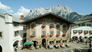 Edificio tradicional con telón de fondo de montaña, que presenta una entrada central y varios ventanales con jardineras.
