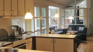 Uma cozinha moderna com uma ilha central, uma área de refeições com sofá e mesa de centro, e grandes janelas que oferecem iluminação natural.