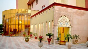 L’entrée d’un hôtel avec une façade en verre, un portail décoré et des plantes en pot.
