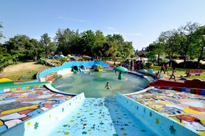 Un parque acuático con toboganes y piscinas, rodeado de árboles y un cielo despejado.