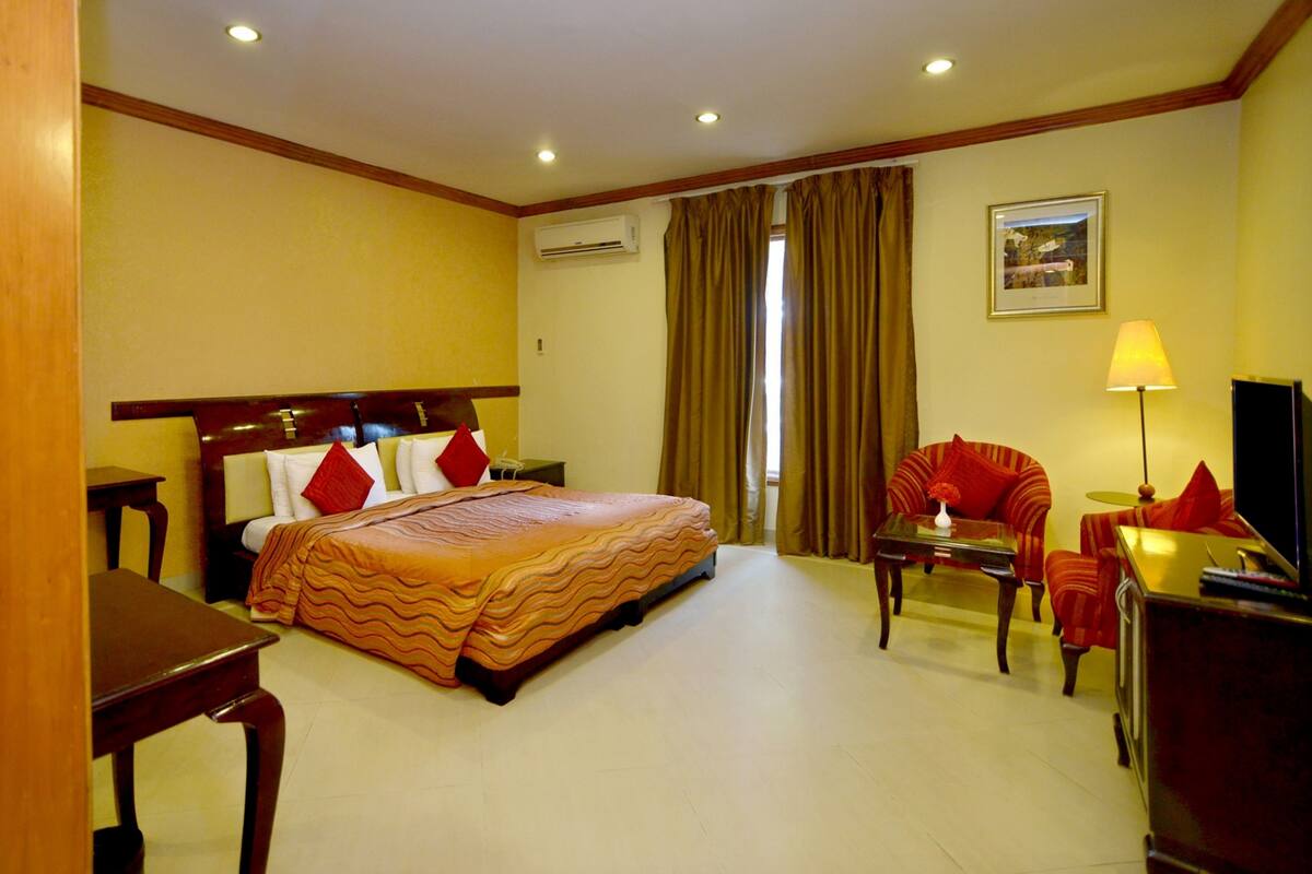 Une chambre d’hôtel avec un lit, un bureau, une chaise, une lampe et un tableau au mur.
