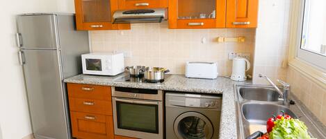 Cocina compacta equipada con refrigerador, microondas, tostadora, horno, lavavajillas y lavadora.