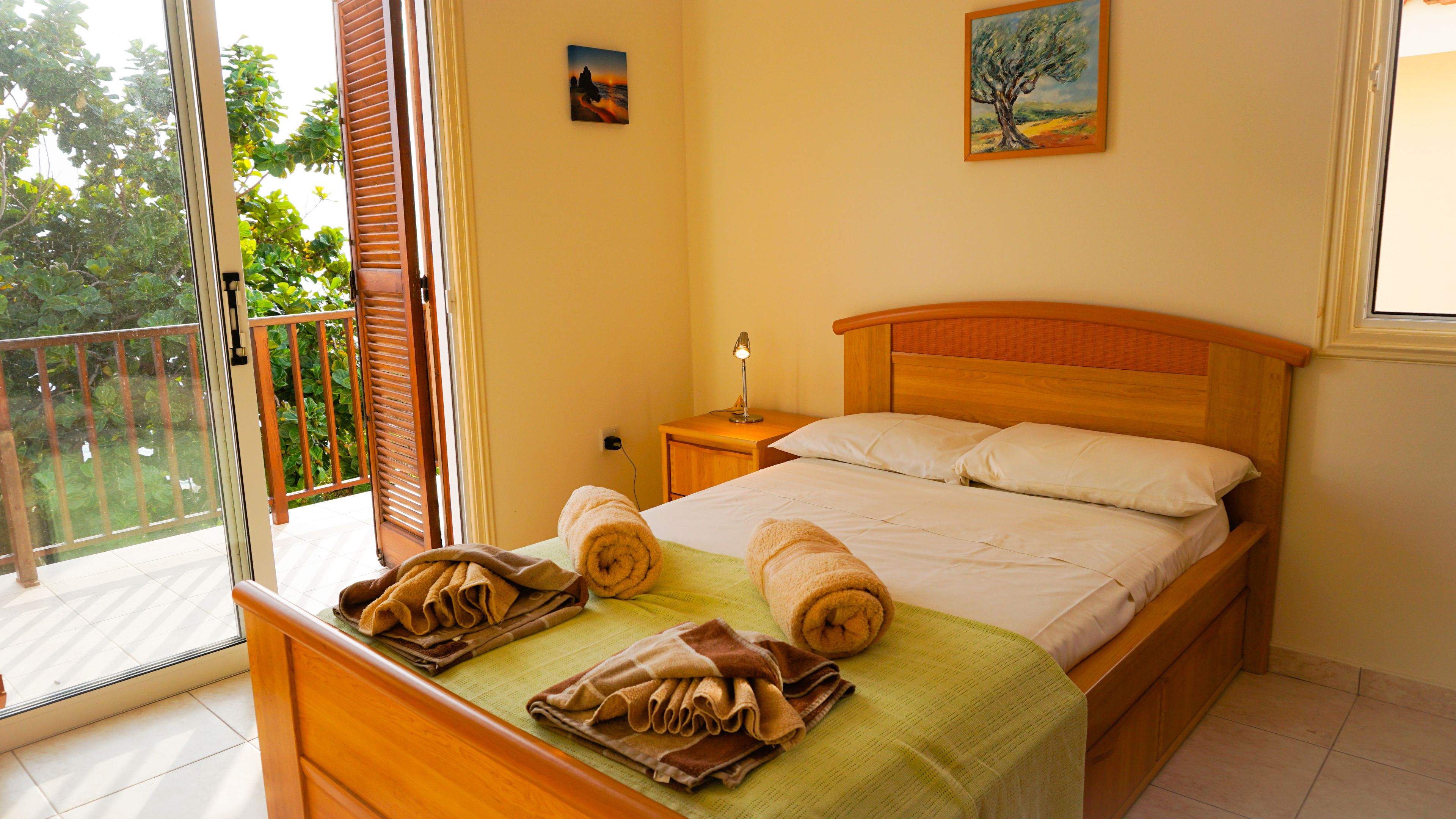 A bedroom with a bed, a nightstand, a lamp, and a view of the outdoors through a sliding door.