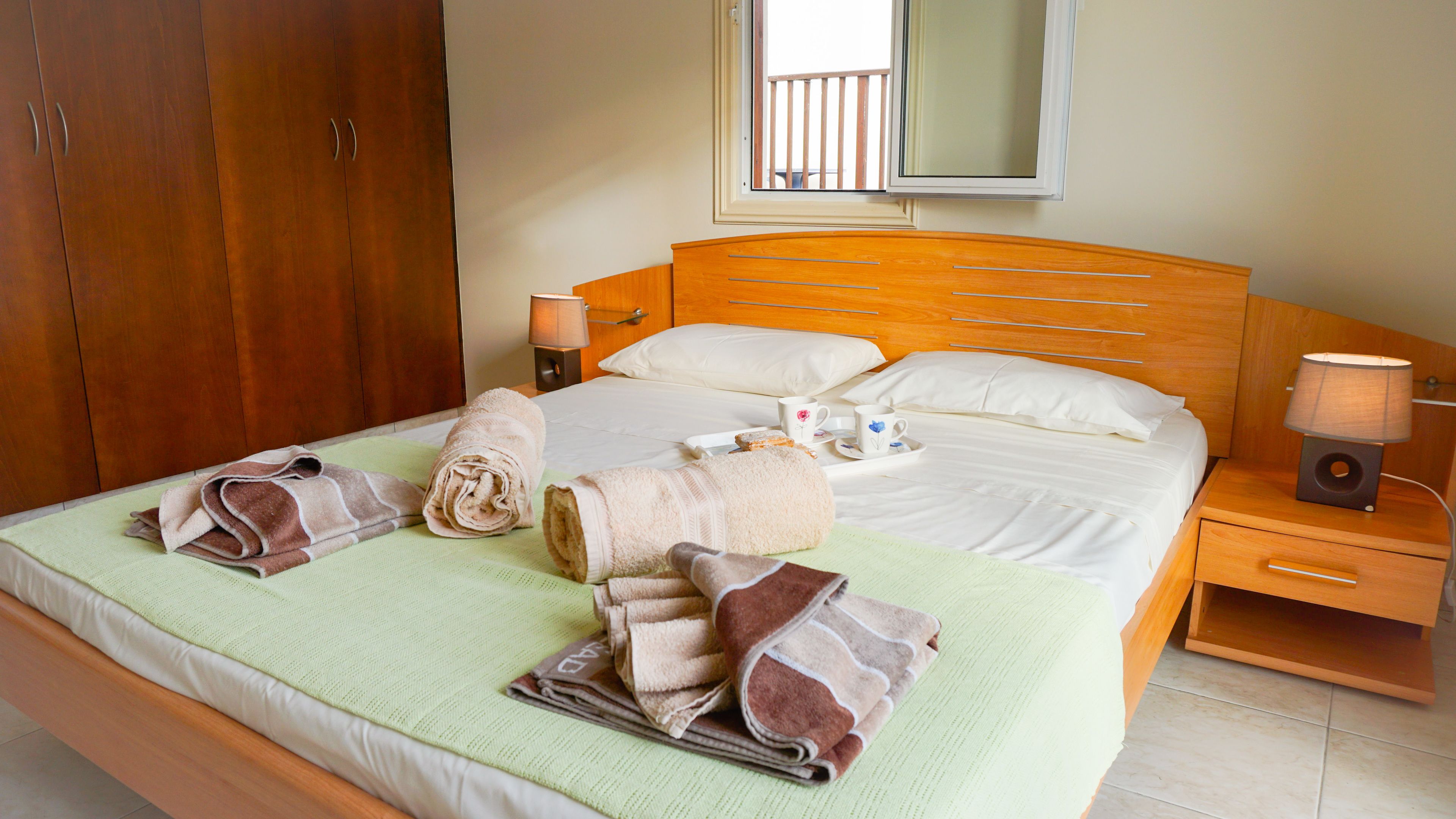 A neatly made bed with towels, a bedside table with a lamp, and a wooden wardrobe.