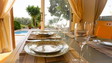 Mesa de comedor dispuesta con platos, vasos y cubiertos, con vistas a una piscina y jardín.