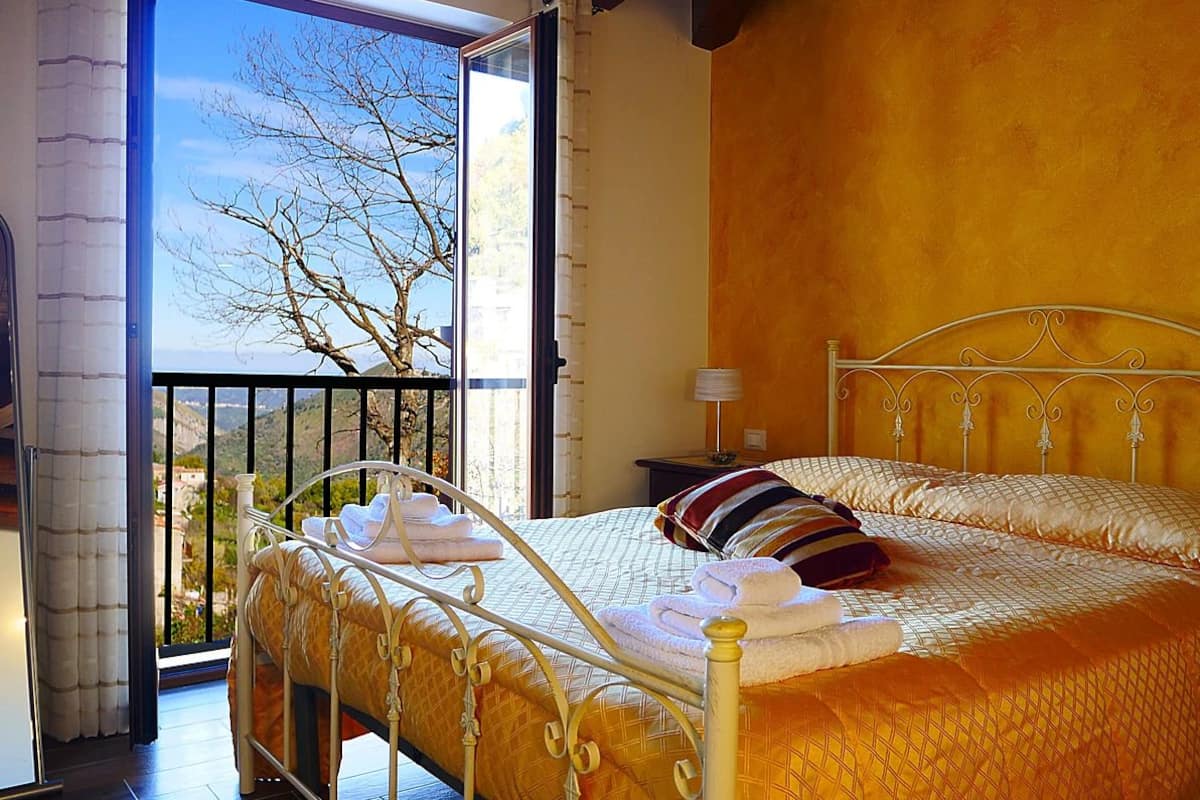 A bedroom with two beds, a balcony with a view of trees, and a window with curtains.