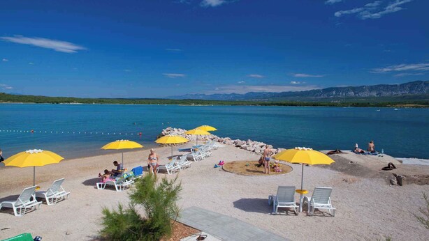 A beach with yellow umbrellas, white lounge chairs, and a clear view of the water and mountains in the background.