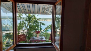 A balcony with a table and chairs, a vase with flowers, and a view of a body of water and greenery.